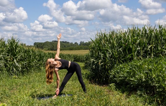 Eine Frau steht in einer Yoga Position neben einem Maisfeld