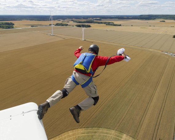 Ein Basejumper springt über einem Feld von einem Windrad.