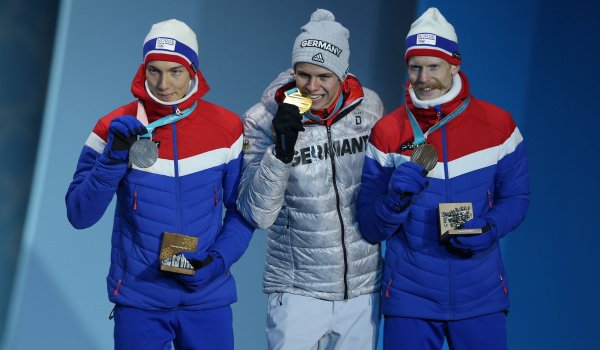 Ja, die Medaille ist echt. Andreas Wellinger, Olympiasieger im Skispringen von der Normalschanze, mit dem obligatorischen Biss in seine Goldmedaille. Mit ihm auf dem Podium die beiden Norweger Johann André Forfang und Robert Johansson 