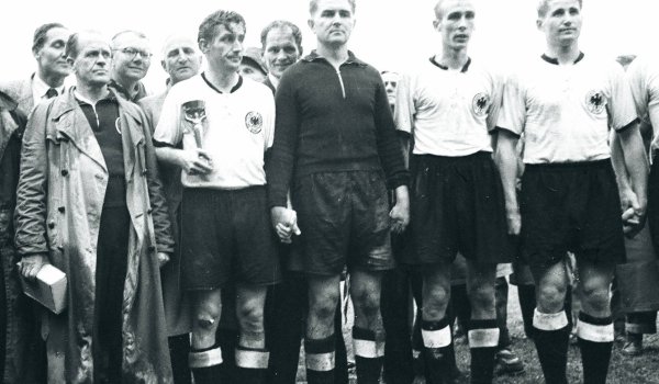 WM 1954: Den ersten WM-Titel schaffte die deutsche Nationalmannschaft noch im traditionellen Look: Fritz Walter (mit Pokal) führte sein Team in weißen Trikots, schwarzen Hosen und schwarzen Stutzen aufs Feld. Zum DFB-Team gehörte auch der Zeugwart Adolf Dassler, der Gründer von Adidas, der im Finale bei Regenwetter Schraubstollen an die Schuhe anbrachte.