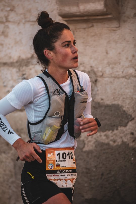 Trailrunnerin Kimi Schreiber beim Laufen; Hintergrund: Steinmauer