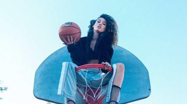 Frau sitzt im Basketballkorb und hält einen Basketball